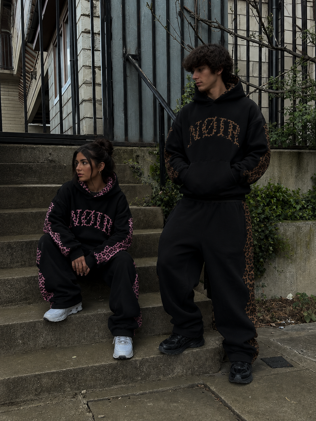 Two people wearing NØIR tracksuits on brownstone steps
